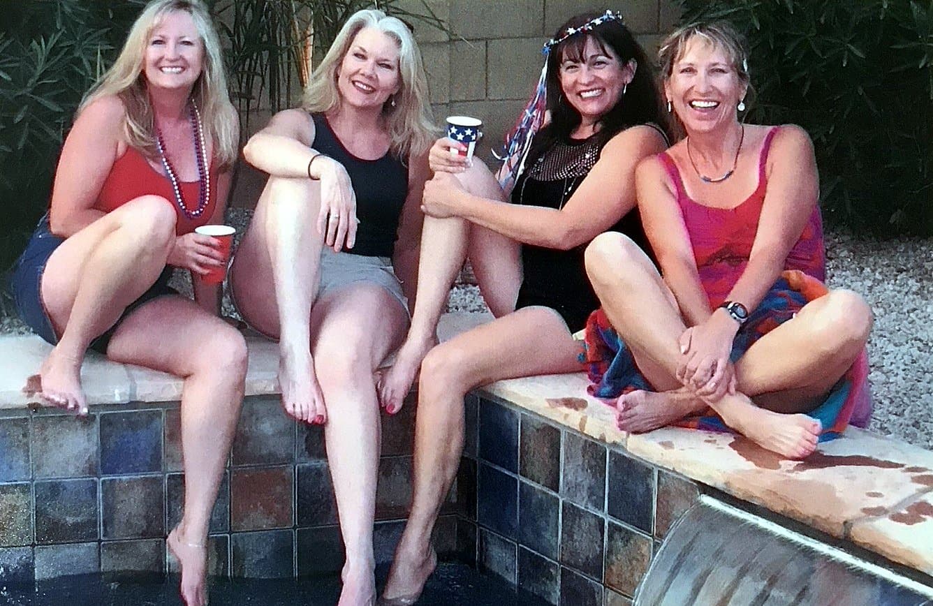 Eve Hess laughing on the edge of a pool with three friends, drinks in hand