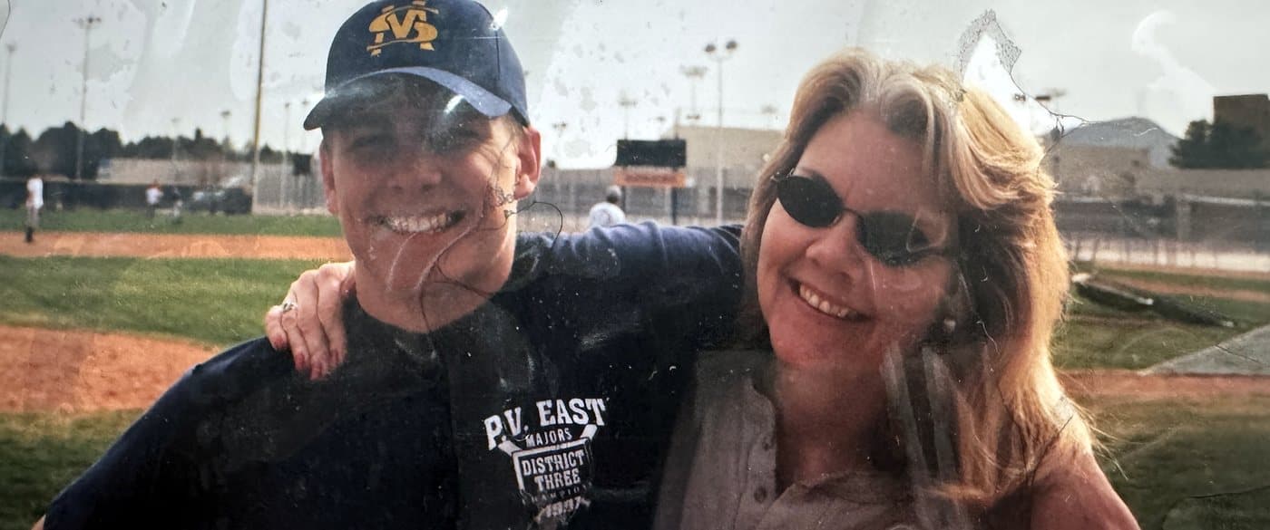 Isaac Hess in a ball cap and Eve Hess in sunglasses, smiling at a baseball field
