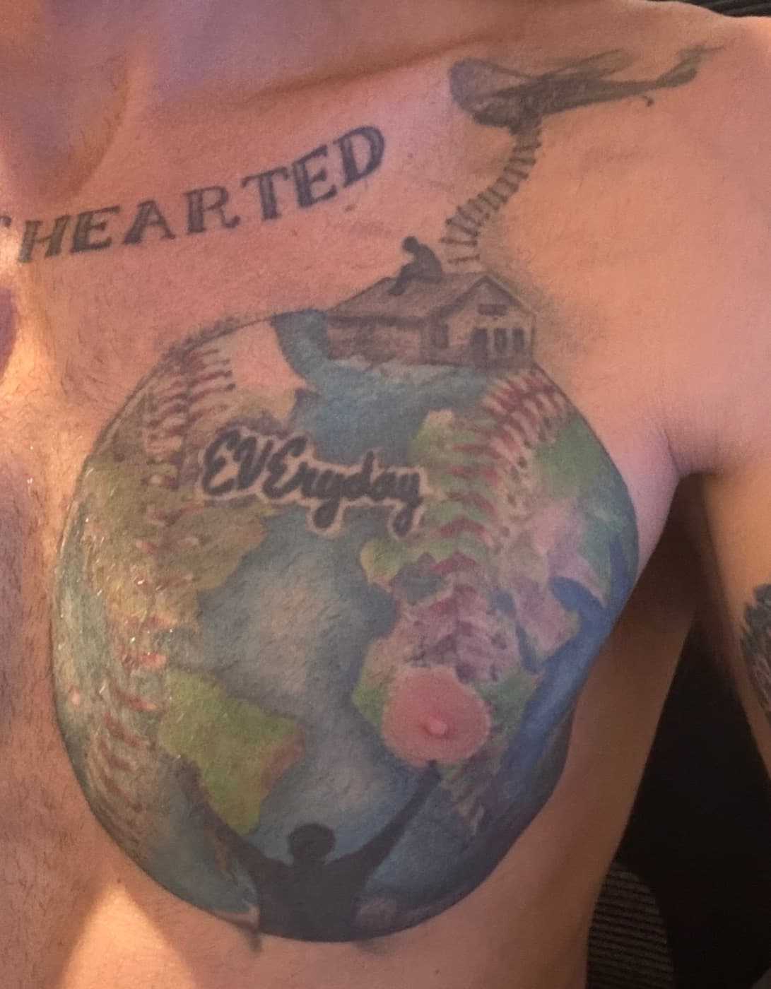 Isaac Hess's chest tattoo: a baseball drawn as the Earth with EVEryday written across it, a boy sitting on a rooftop above it with a helicopter and rope ladder over him, and a person with arms raised below
