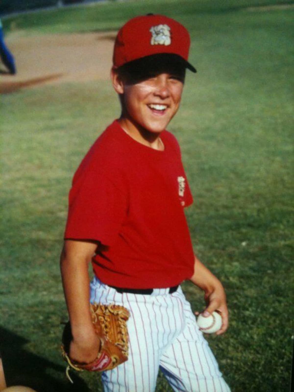 Isaac Hess as a kid in a red cap and pinstripes, glove and ball in hand, grinning
